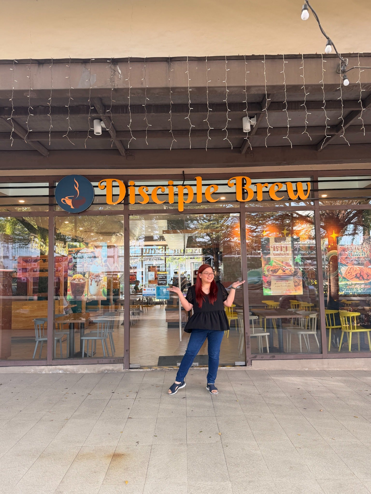 Trixie smiling outside Disciple Brew beneath the café sign